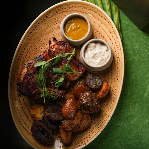 Grilled chicken with roasted potatoes and two dipping sauces on an oval plate.