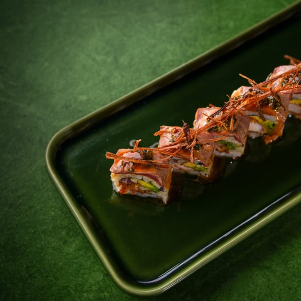 Mikhuna Japanese-Peruvian sushi rolls with seared beef, avocado, and crispy toppings on a green plate.
