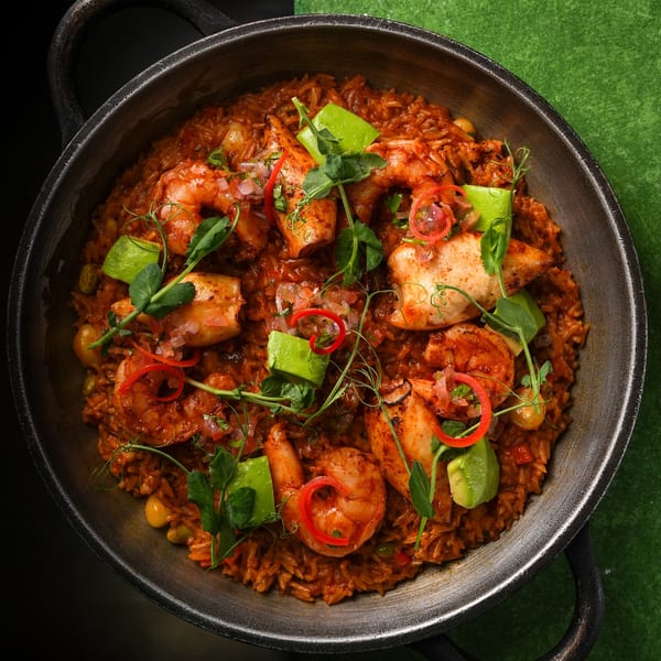 Mikhuna's Japanese-Peruvian seafood rice dish with shrimp, squid, avocado, and red chili in a pan.