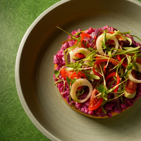 Vibrant purple salad with red peppers, white onion rings, and green sprouts in a gray bowl.