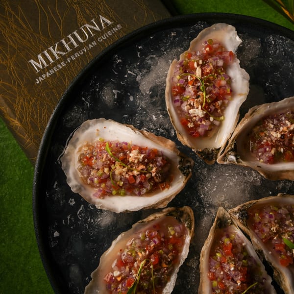 Mikhuna Japanese-Peruvian Cuisine oysters on the half shell with diced red onion, tomato, and herbs.