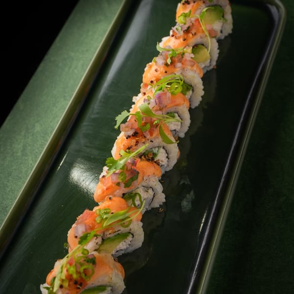 Mikhuna Japanese-Peruvian Cuisine's sushi roll with salmon, avocado, and herbs on a dark green plate.