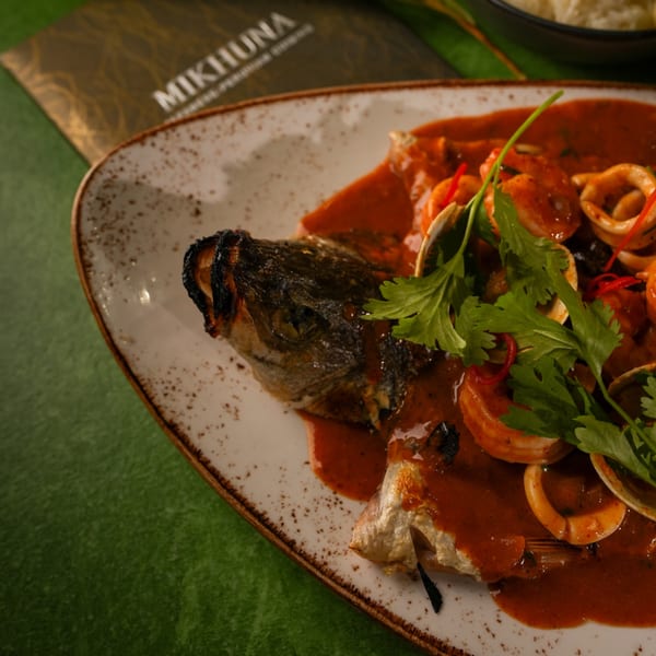 Whole grilled fish with head and tail, covered in red sauce with seafood and cilantro.